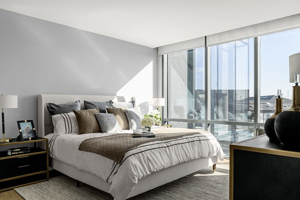 Interior photo of a typical bedroom in an apartment at RVR showing a queen sized bed with 2 night stands with dramatic floor to ceiling windows.,