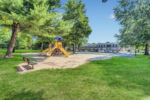 A playground with a yellow slide and a bench in the foreground.