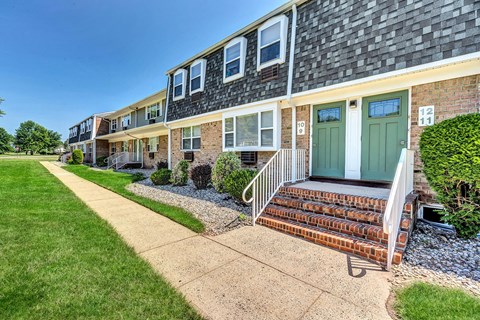 Exterior photo of Beekman Gardens in Hillsborough, NJ showing a beautiful apartment building, with brick stairs leading to the entry doors. A sidewalk and lush landscaping can be seen in front of the building.
