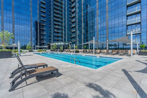 Exterior photo of the community’s pool located on the 5th floor at RVR showing a large pool surrounded by multiple shaded seating with patio chairs overlooking the community’s building.