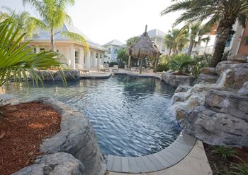 a large swimming pool with a rock waterfall and a thatched hut in the background