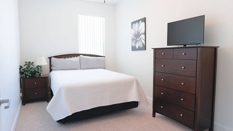 A bedroom with a bed, nightstand, and a dresser with a television on top.