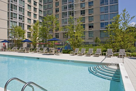 A swimming pool with lounge chairs and umbrellas in front of a large building.