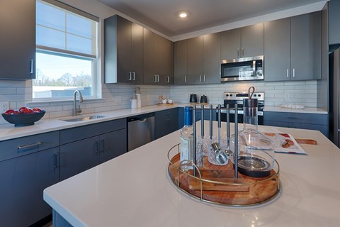 A kitchen with a white counter top and a wooden cutting board on it.