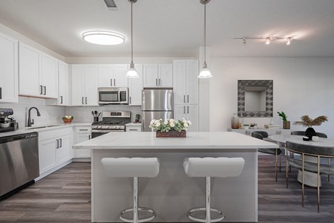 a kitchen with white cabinets and a large island with white chairs