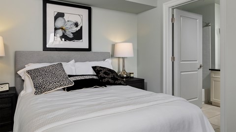 A cozy, well-appointed bedroom with a grey upholstered headboard and direct access to an en-suite bathroom in these luxury Rittenhouse Square apartments Philadelphia PA.