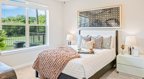 A bedroom with a large bed and a view of a fence and trees outside the window.