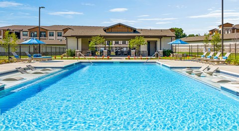 A large swimming pool in front of a building with a fence and umbrellas.