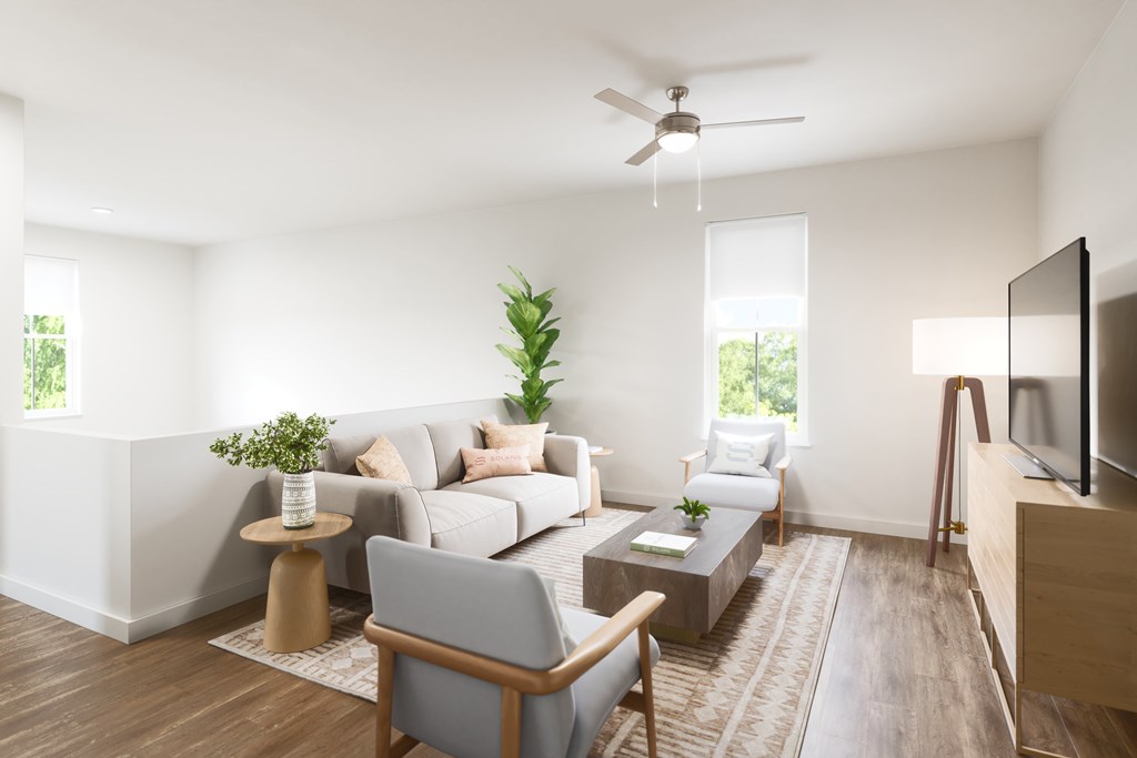 A living room with a grey couch, a small table, a television and a plant.