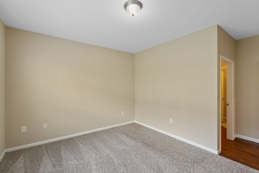 an empty living room with carpet and a door to a hallway