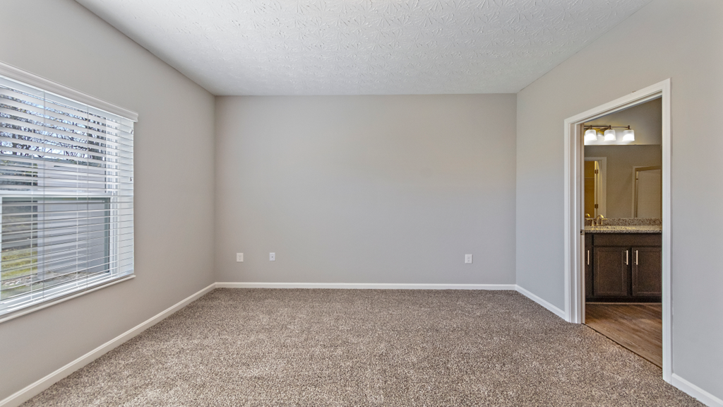 an empty bedroom with a large window and a carpeted floor