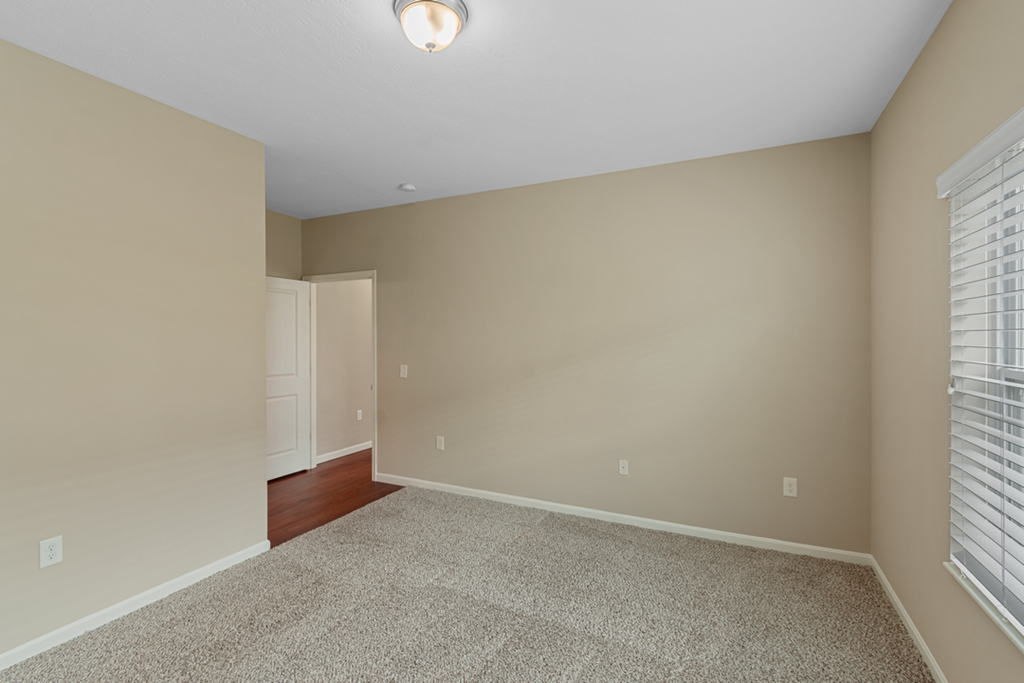 an empty living room with beige carpet and a window