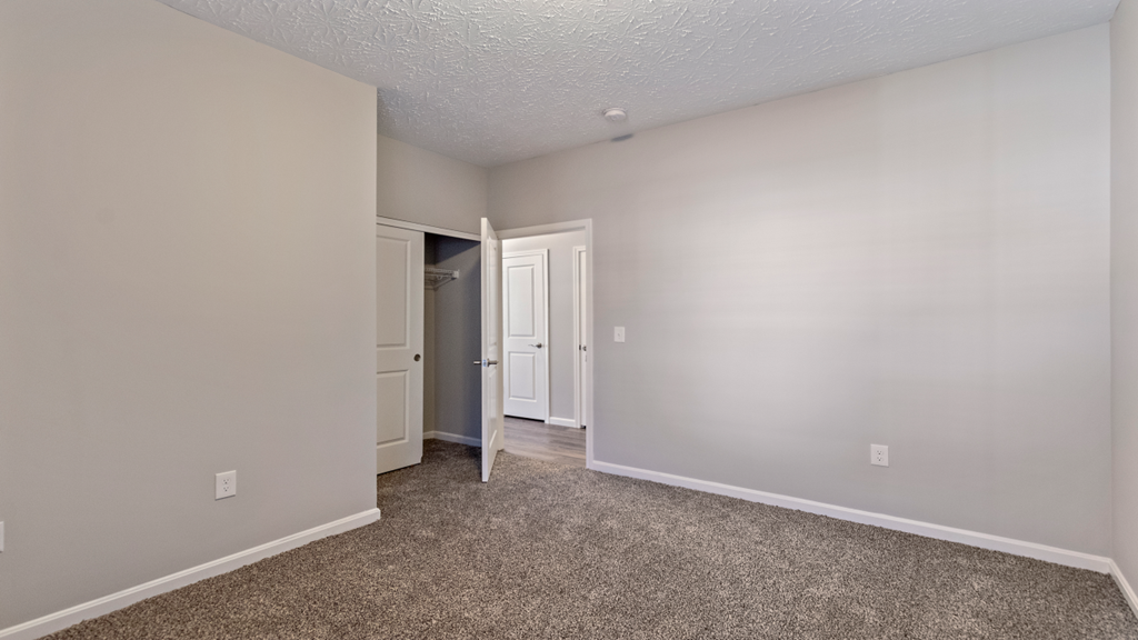 a bedroom with white walls and carpet and a door to a closet
