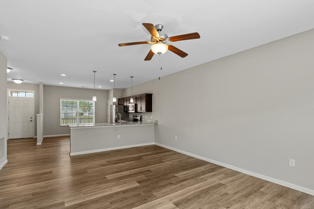 an empty living room with a ceiling fan and a kitchen