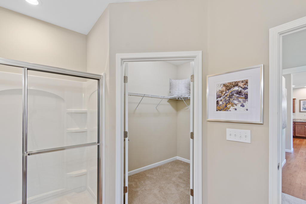 a walk in closet with a mirrored closet door and a door to a shower