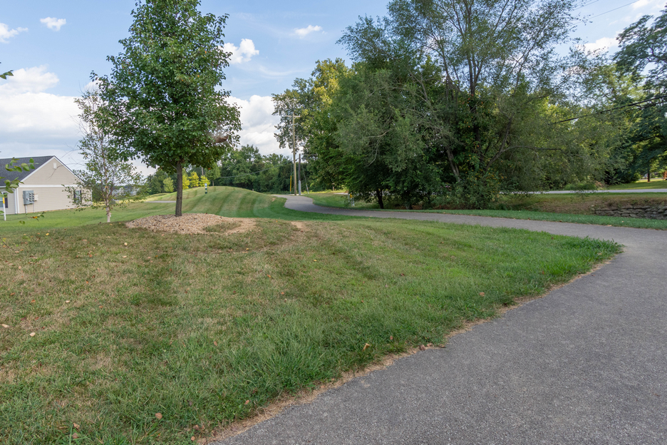 A paved walkway curves through a grassy area with trees in the background.