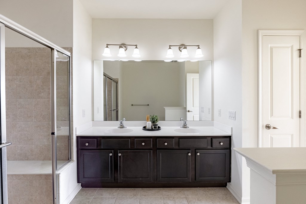 Modern bathroom featuring a double vanity with dark wood cabinets, large mirror, and a tiled walk-in shower at Queens Gate Apartments.