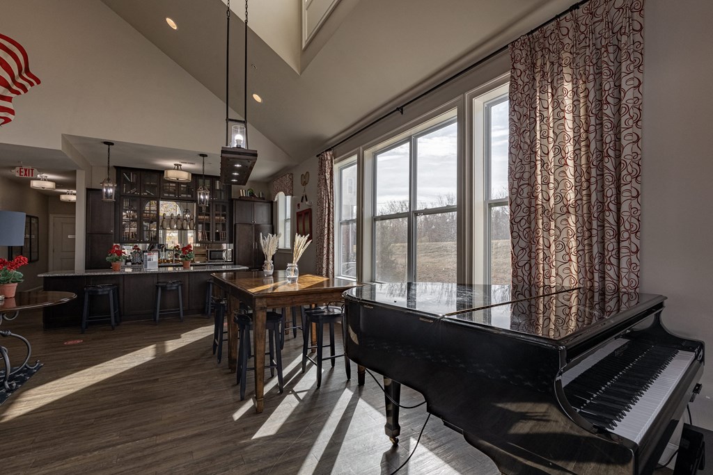 Elegant clubhouse at Queens Gate Apartments featuring natural light, a grand piano, communal dining tables, and a modern bar area.