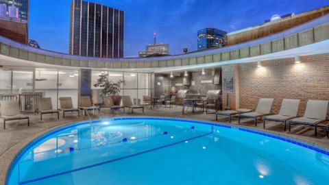 A swimming pool with chairs around it in a room with a brick wall.