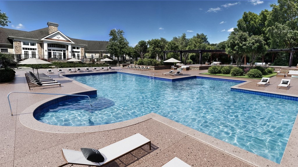 A large swimming pool with a hot tub and lounge chairs.