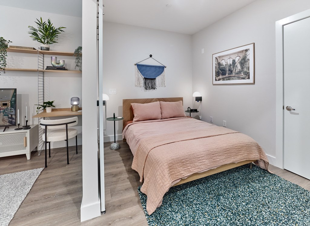 Chic bedroom area in a studio apartment at The Mint Rahway, featuring a comfortable bed, workspace, and stylish decor.