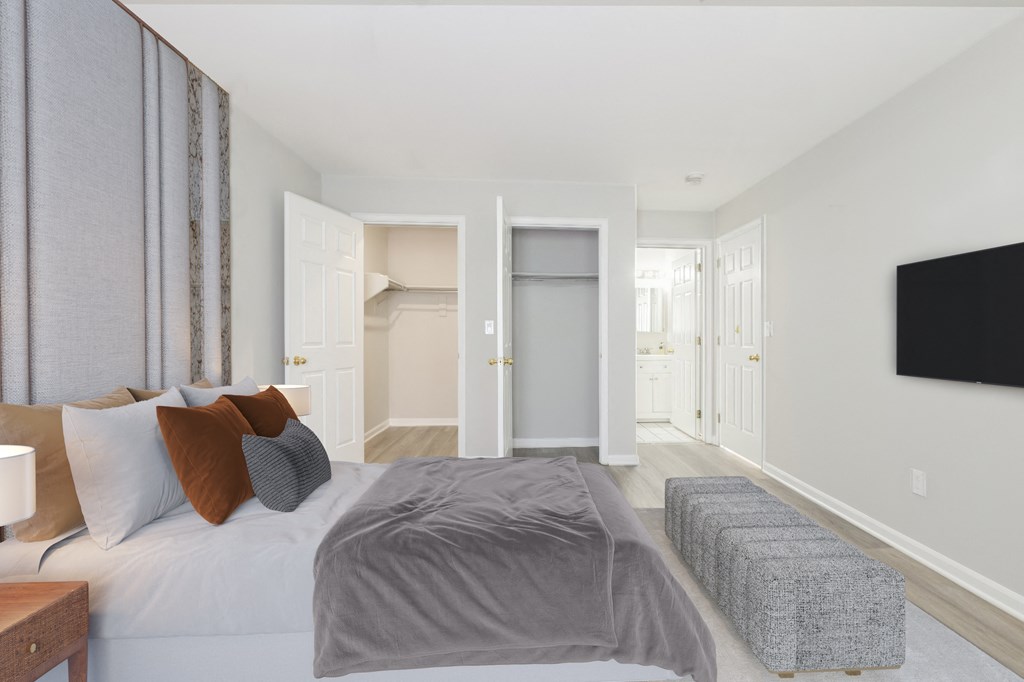 A well-lit bedroom with open closet space at The Village at Bridgewater in Bridgewater, NJ. Highlights include neutral tones, wood-style flooring, and an ensuite bathroom.