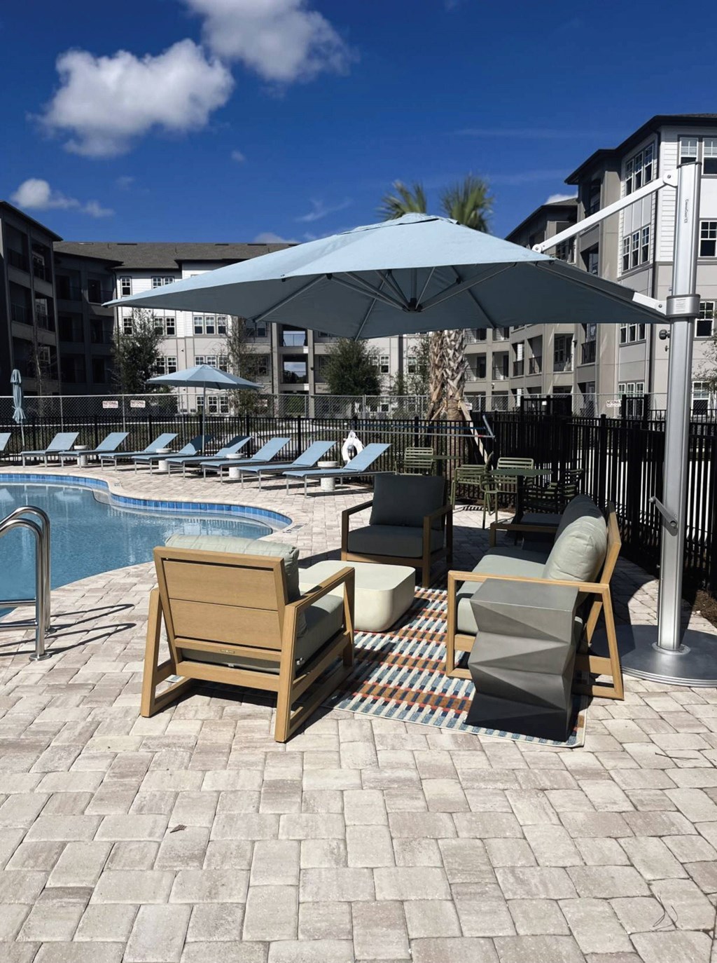 A patio with a pool and chairs under an umbrella.