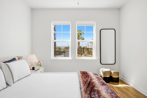 A bedroom with a large bed and a window overlooking a fence and trees.