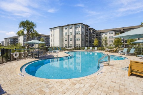 A swimming pool surrounded by a tiled patio and lounge chairs.
