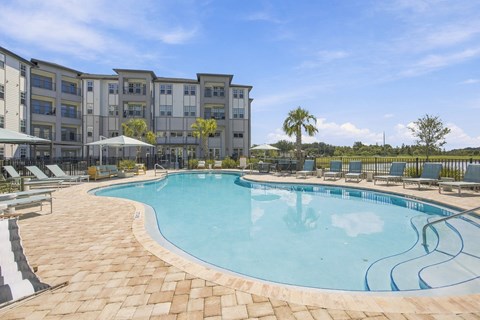 A swimming pool surrounded by a tiled patio and lounge chairs in front of a building.