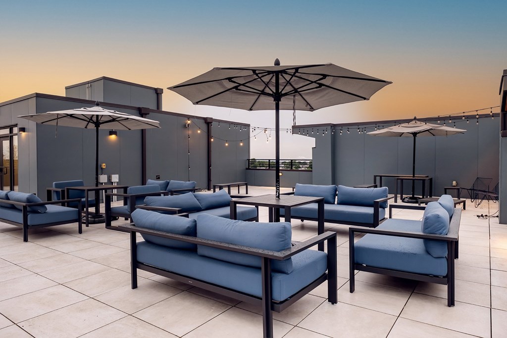 Rooftop terrace with blue cushioned seating, umbrellas, and string lights at The Botanic in Carteret, NJ