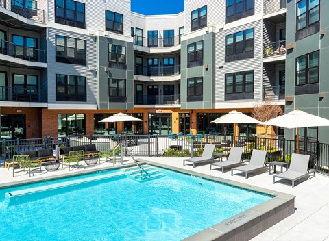 a swimming pool in front of a building with chairs and umbrellas