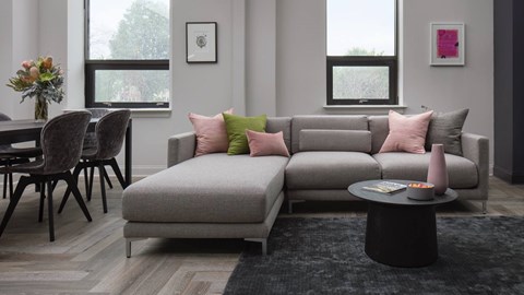 A grey couch with pink and green pillows sits in a living room.