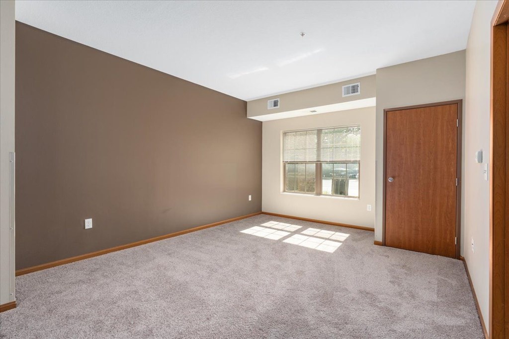 A large, empty room with a carpeted floor and a window with blinds.