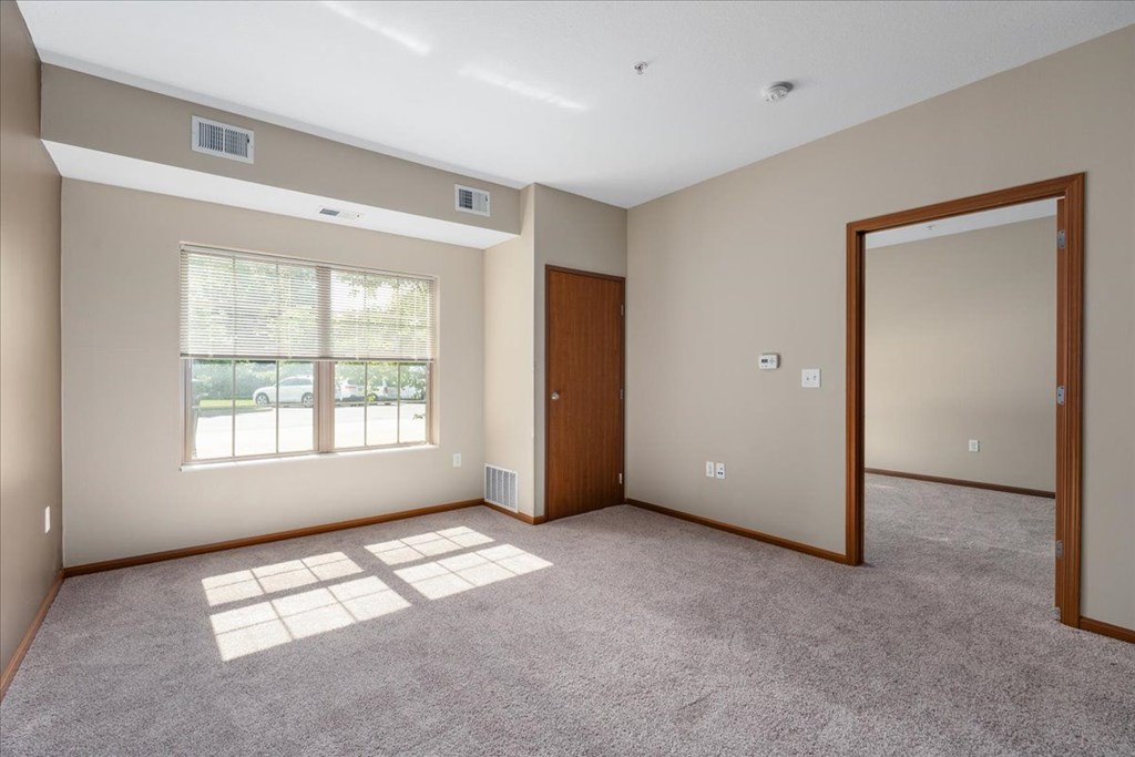 A room with a carpeted floor and a window with blinds.