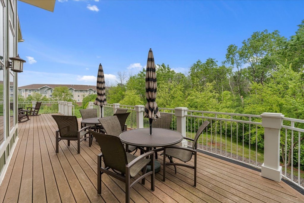 A wooden deck with a table and chairs and two striped umbrellas.