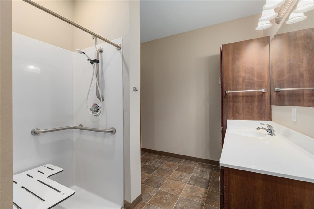A bathroom with a white shower, brown cabinets, and a white sink.