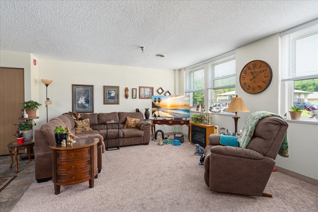 A living room with a brown couch, a brown chair, and a clock on the wall.