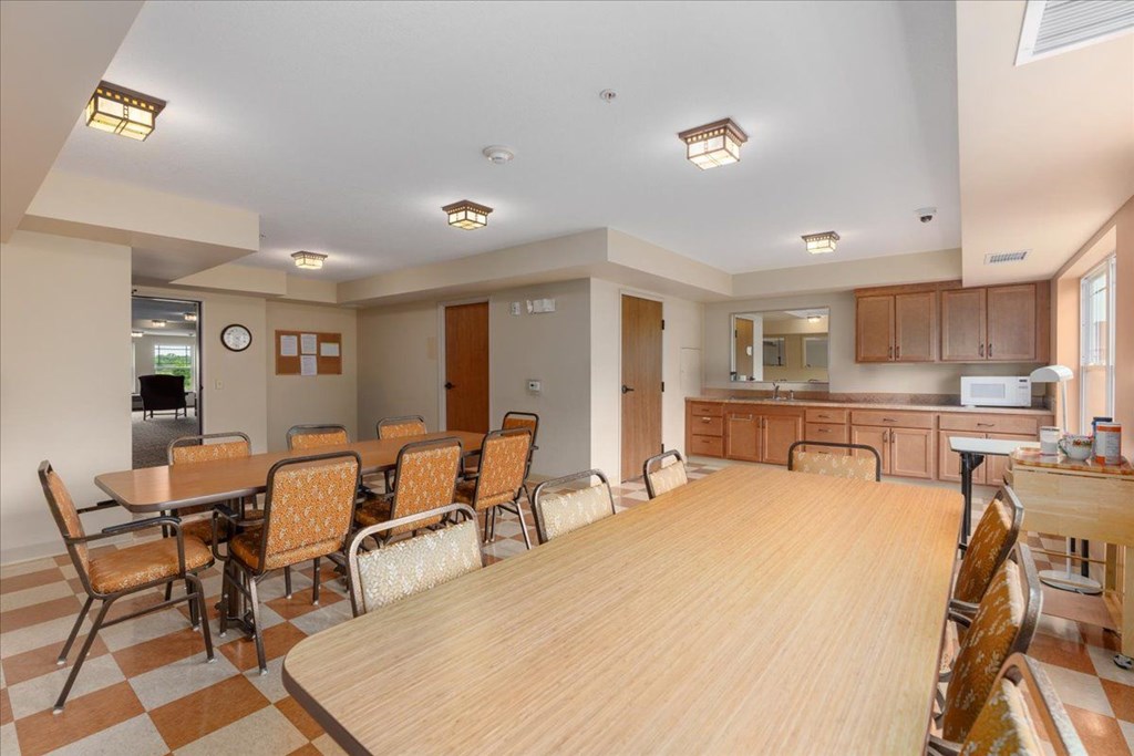 A kitchen with a table and chairs in the foreground and a counter top with a microwave.