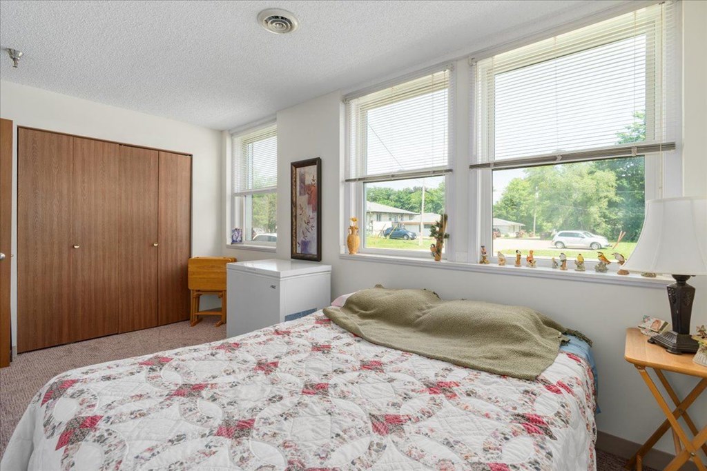 A bedroom with a bed, a nightstand, a window, and a wooden wardrobe.
