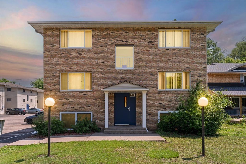 A brick house with a blue door and windows with curtains.