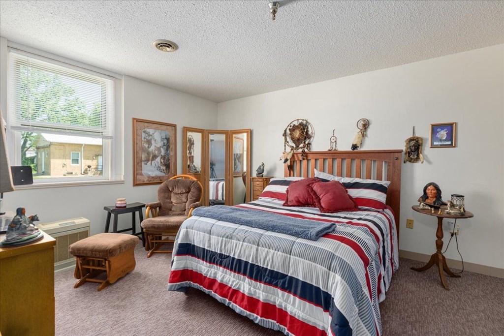 A bedroom with a bed, chair, and a window.