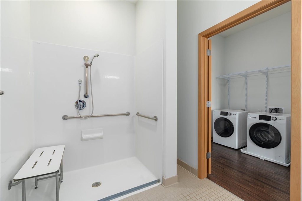 A bathroom with a walk in shower and a washer and dryer in the doorway.