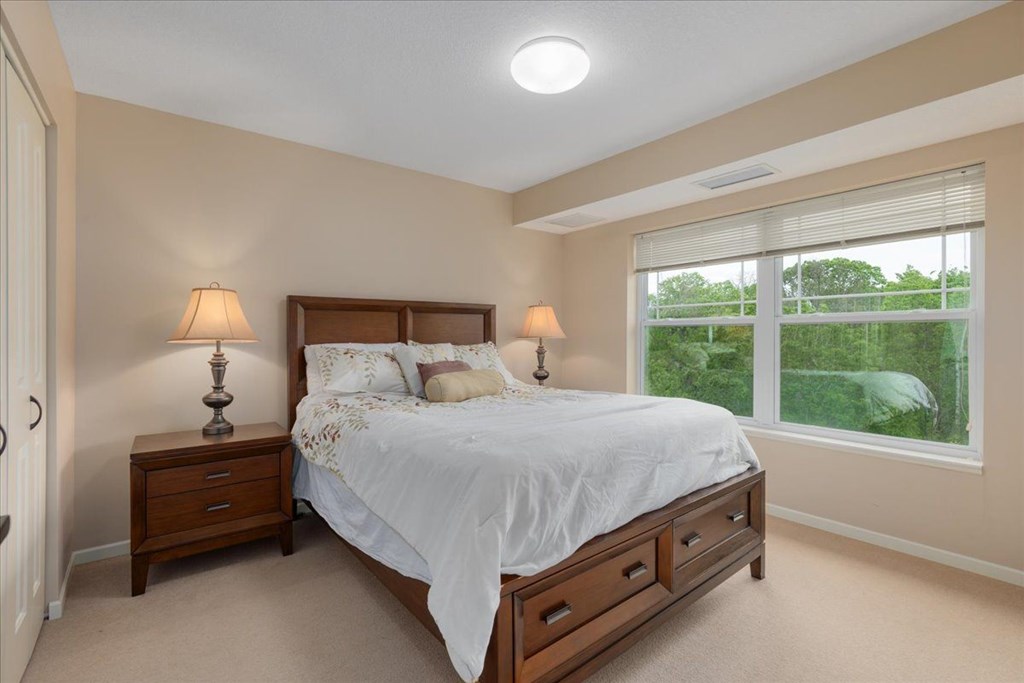 A bedroom with a bed, nightstands, and a window overlooking a green landscape.