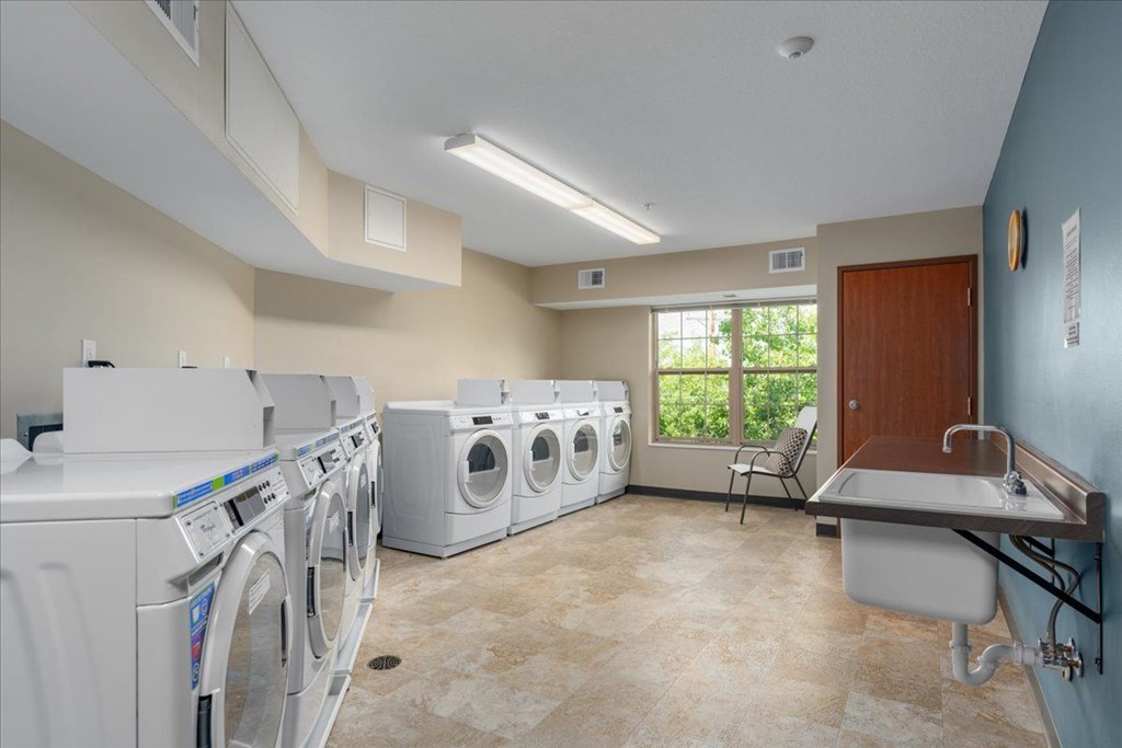 A laundry room with a row of washing machines and a sink.
