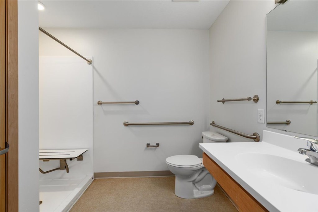 A white bathroom with a toilet, sink, and grab bars.