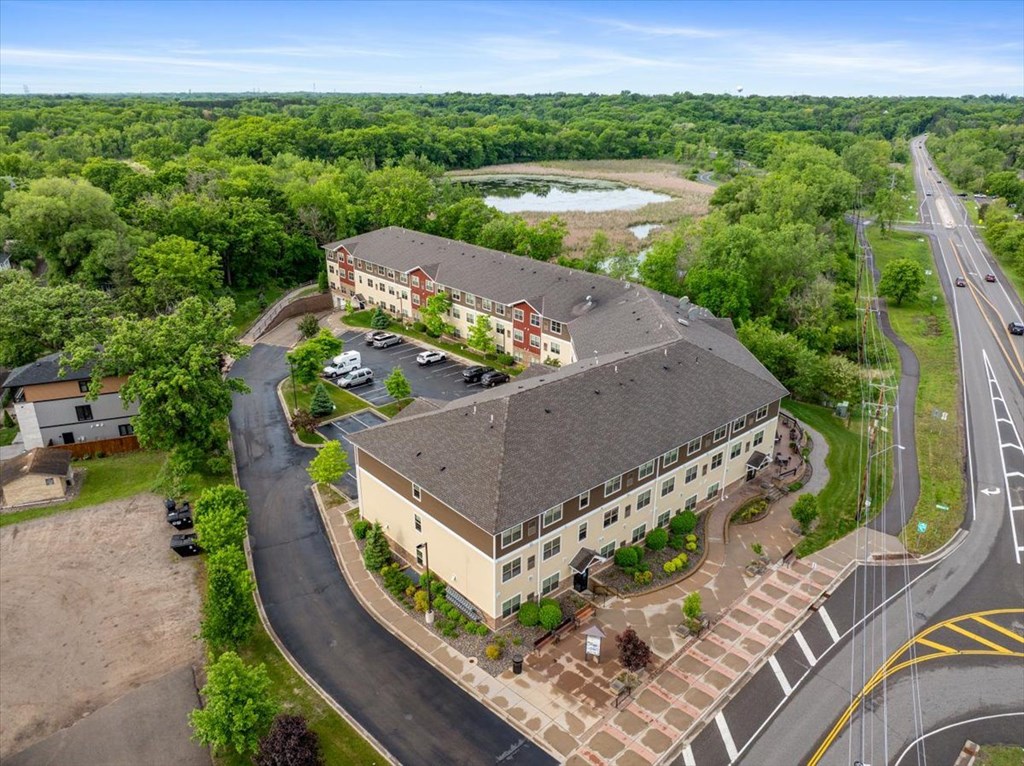 A large building with a red roof is surrounded by trees and a parking lot.
