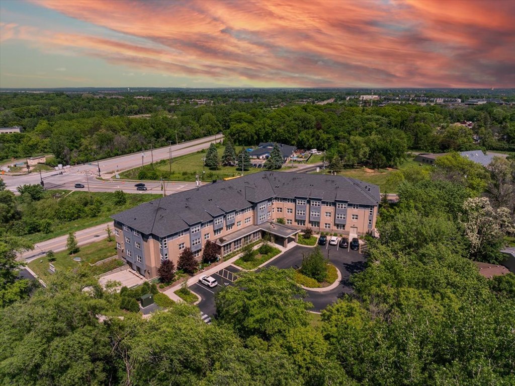 A large building surrounded by trees with a parking lot in front.