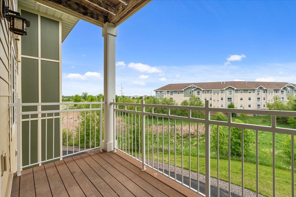A balcony with a white railing overlooks a grassy area and apartment buildings.