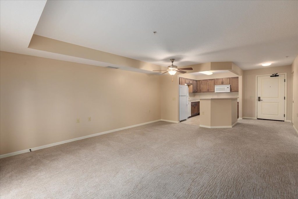 Empty room with a ceiling fan and a kitchenette in the background.